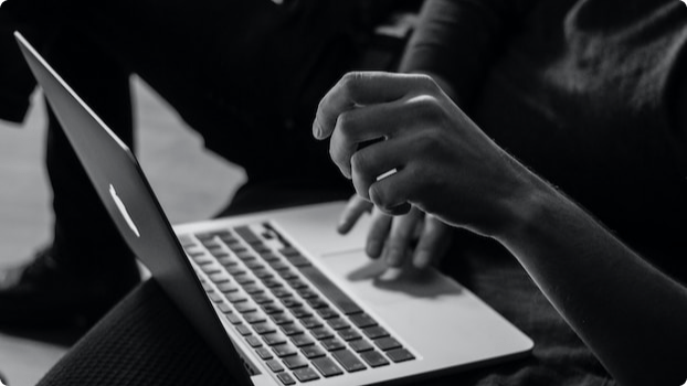 Laptop open on figure's lap with hands present