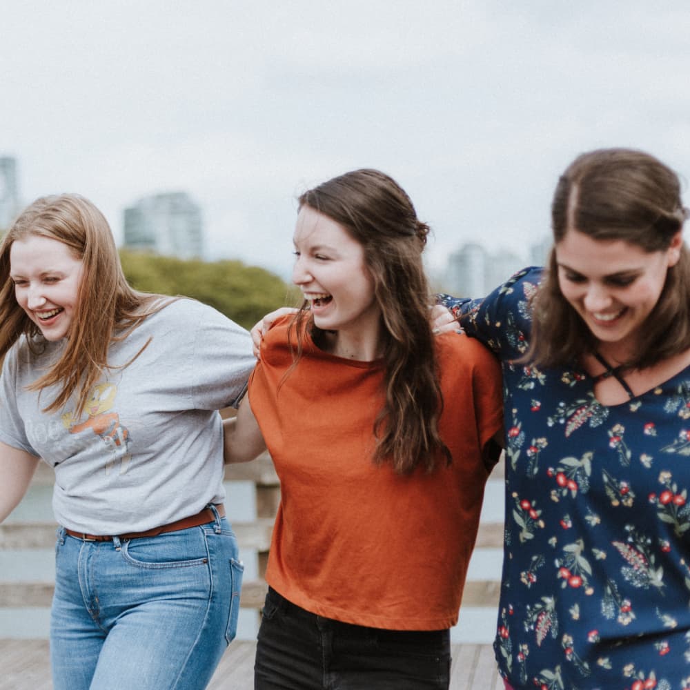 Three young women crossing arms and laughing while walking.