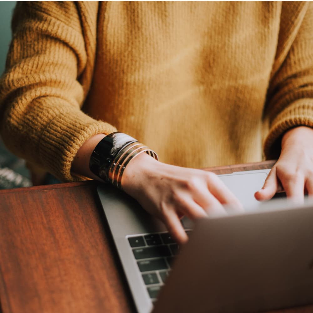 Person typing on laptop on wooden table.