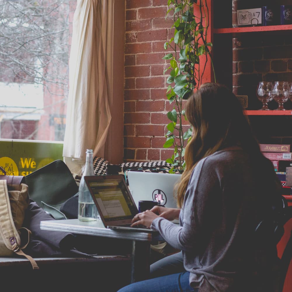 Woman typing on laptop near a window indoors.